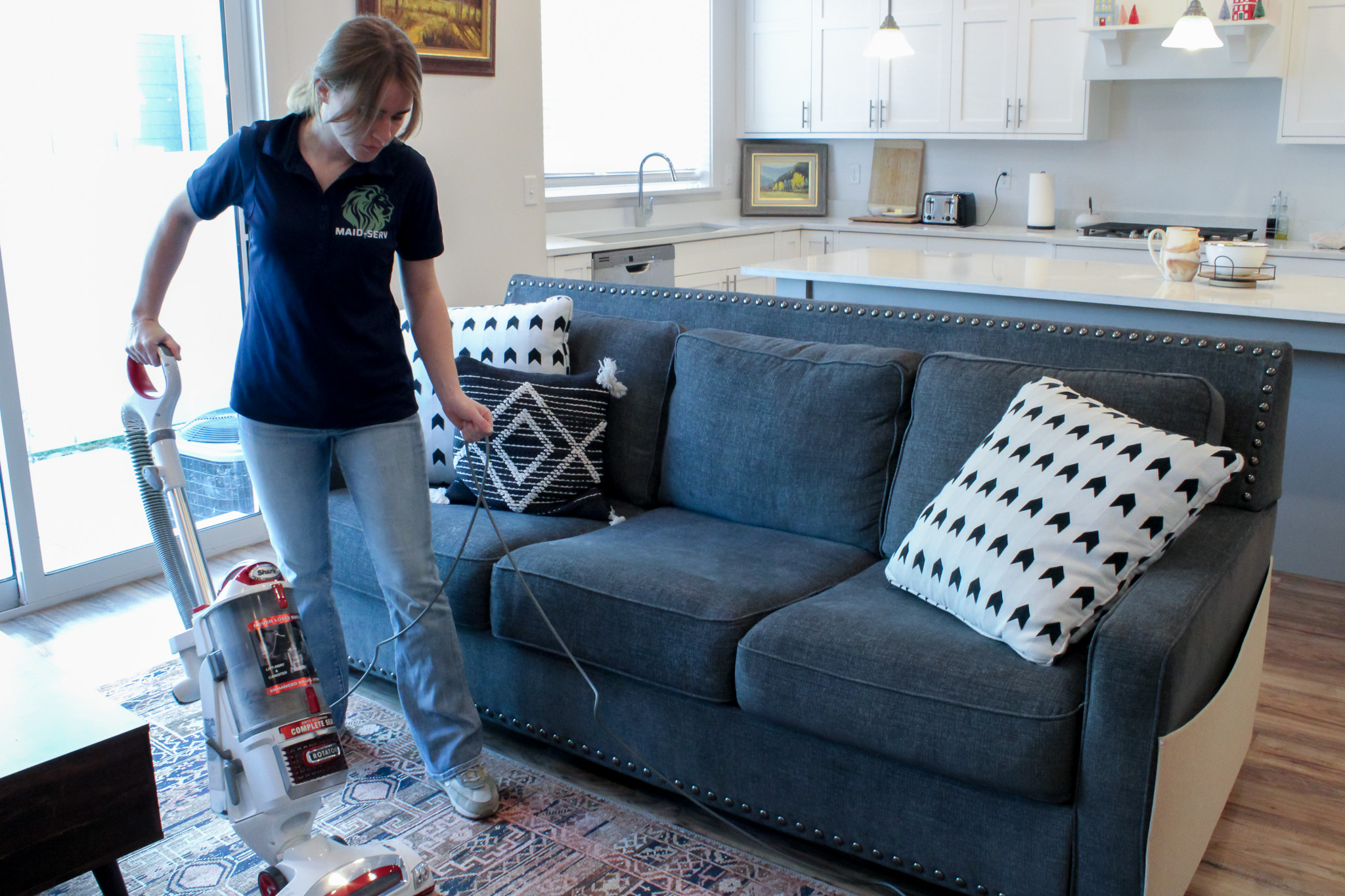 woman cleaning living area, vacuuming rug for cleaning services. Maid-Serv residential and home cleaning services